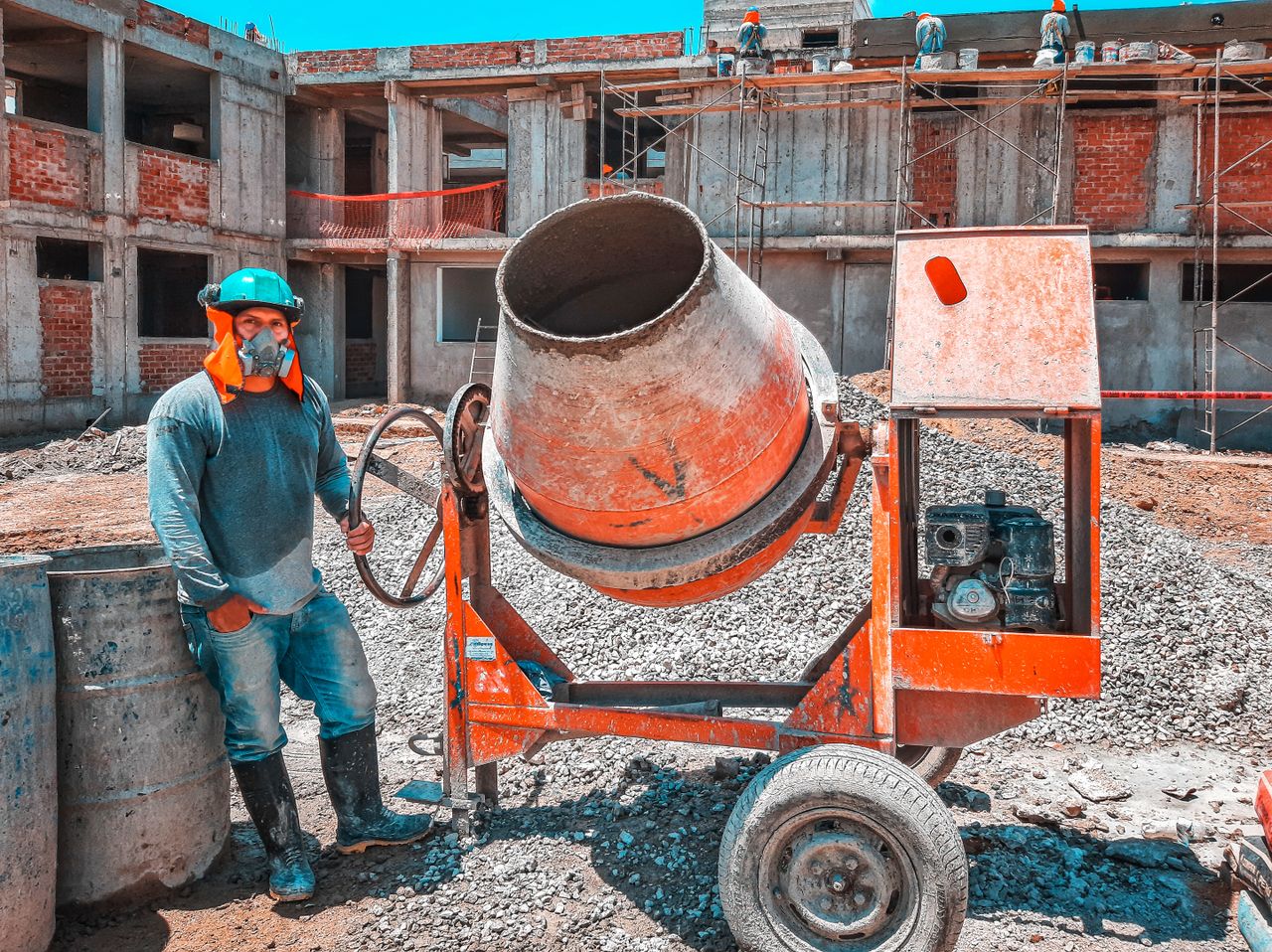 About A construction worker operating a concrete mixer at an active building site, emphasizing safety gear.